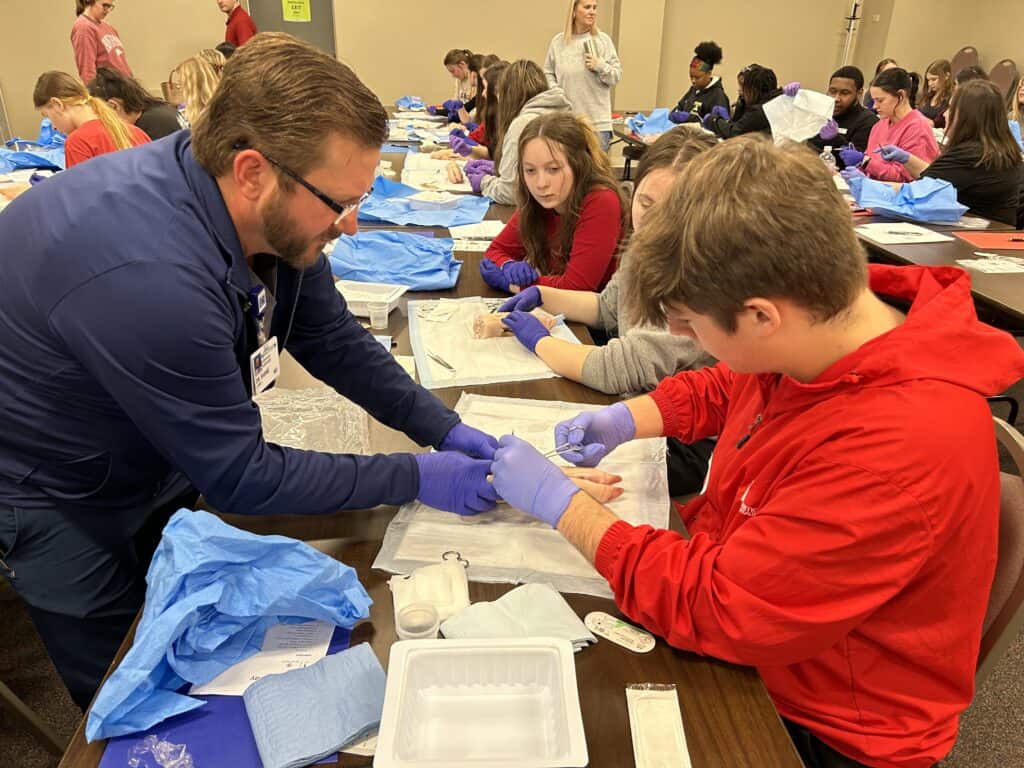 Dr. Shane Lyerly assists high school students with a suturing activity during UAMS Northeast A Day in the Life event.